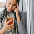 Woman, hand on head, confused expression, looking at orange iPhone  