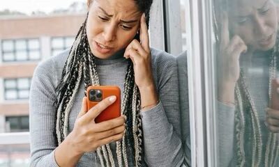 Woman, hand on head, confused expression, looking at orange iPhone  