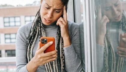Woman, hand on head, confused expression, looking at orange iPhone  
